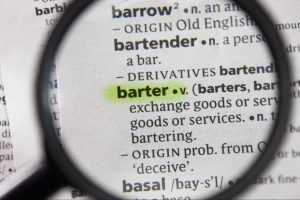 Lupa focando na palavra 'barter' em um dicionário de papel, com marca texto por cima.