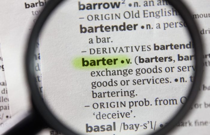 Lupa focando na palavra 'barter' em um dicionário de papel, com marca texto por cima.