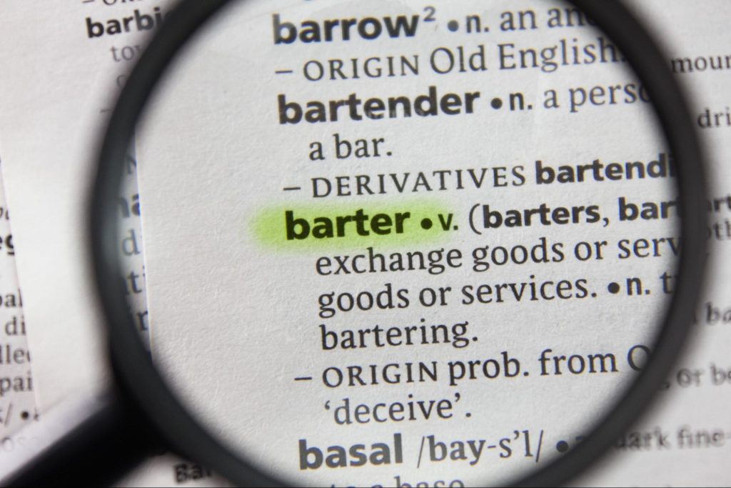 Lupa focando na palavra 'barter' em um dicionário de papel, com marca texto por cima.