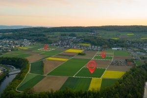 Imagem aérea de terras agrícolas demarcadas por traçados e linhas, com ilustrações digitais de símbolos de localização em alguns lotes.