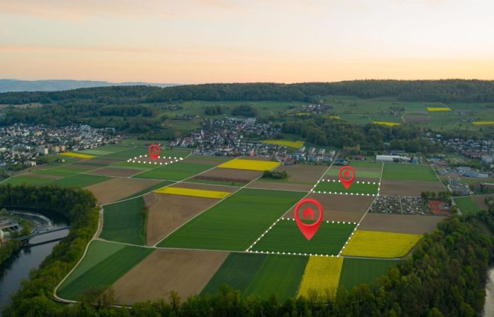 Imagem aérea de terras agrícolas demarcadas por traçados e linhas, com ilustrações digitais de símbolos de localização em alguns lotes.
