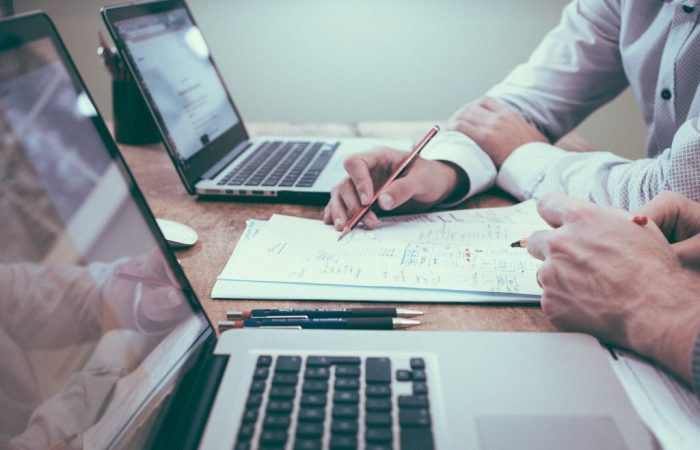 Dois homens usando notebook e analisando documentos físicos, simbolizando antecipação de recebíveis