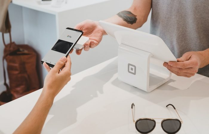 Atendente usando computador no caixa de loja e pessoa segurando celular para pagar, simbolizando NFC-e