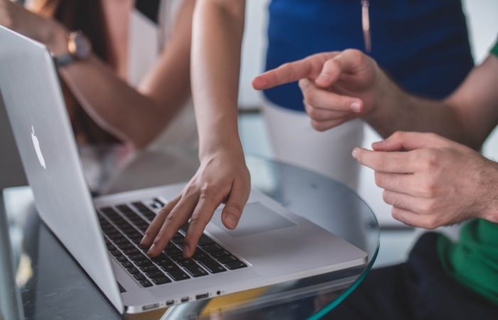 Três pessoas apontando e usando notebook, simbolizando nota fiscal eletrônica e de produto