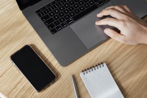 Pessoa usando notebook com celular e bloquinho de notas com caneta ao lado, simbolizando Difal ICMS