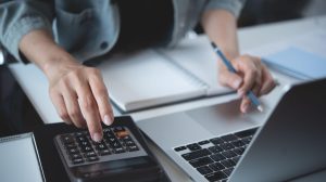 pessoa usando notebook e calculadora para saber como calcular imposto de nota fiscal
