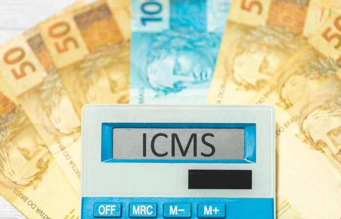 calculadora de ICMS e alíquotas interestaduais. Ao fundo da imagem, notas de dinheiro