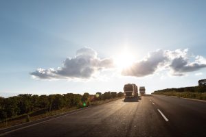 Dois caminhões em uma rodovia, com plantações em ambos os lados da via.
