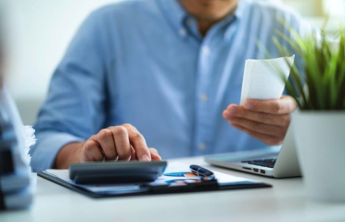 Homem segurando papel com a mão esquerda e utilizando calculadora com a mão direita, para emitir a NFSe.